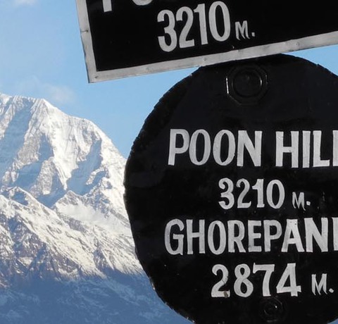 Blick auf den schneebedeckten Poon Hill in Nepal mit einem Wegweiser im Vordergrund