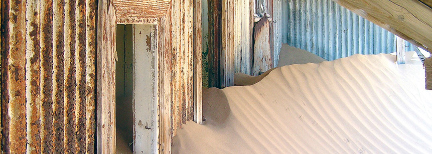 Blick in ein verlassenes Haus in Luederitz in Namibia, das inzwischen schon zu einem großen Teil mit Sand befüllt ist, den der Wind durch die offenen Türen und Fenster getragen hat