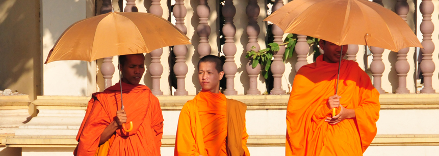 Drei Mönche in orangen Roben mit Sonnenschirmen auf einer Laos Rundreise
