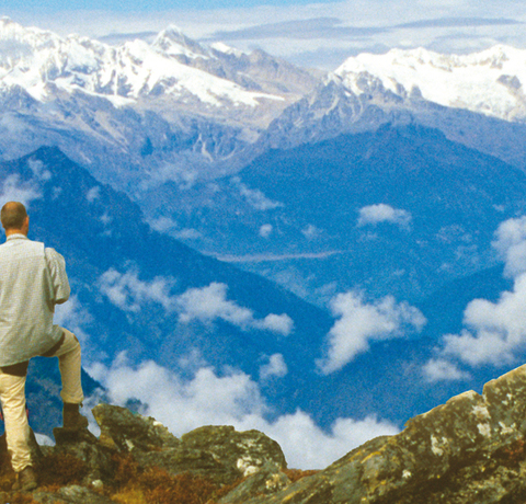 Vier Wanderer blicken von einem Aussichtspunkt auf das Langtang Tal während einer Nepal Reise mit schneebedeckten Eisriesen des Himalaya Gebirges am Horizont