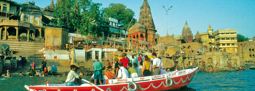 Blick auf die Ghats von Varanasi in Indien am Ganges mit Pilgern und einem Boot im Vordergrund