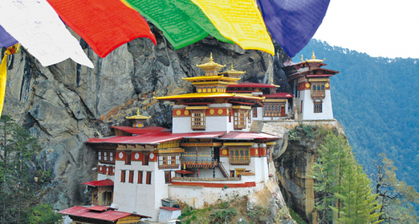 An den Berg geschmiegtes Tigernest Kloster in Bhutan mit Gebetsfahnen im Vordergrund