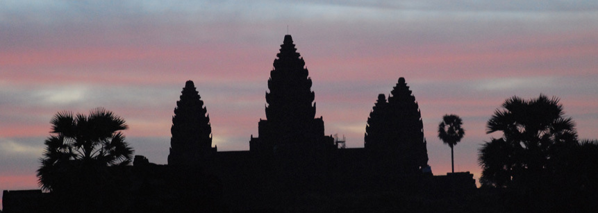 Hinter dem Tempel von Angkor Wat in Kambodscha geht langsam die Sonne auf und färbt den Himmel rot.