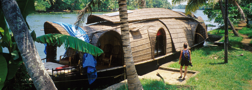 Kleines Hausboot in den Backwaters von Kerala auf einer Indien Reise mit Palmen im Vordergrund